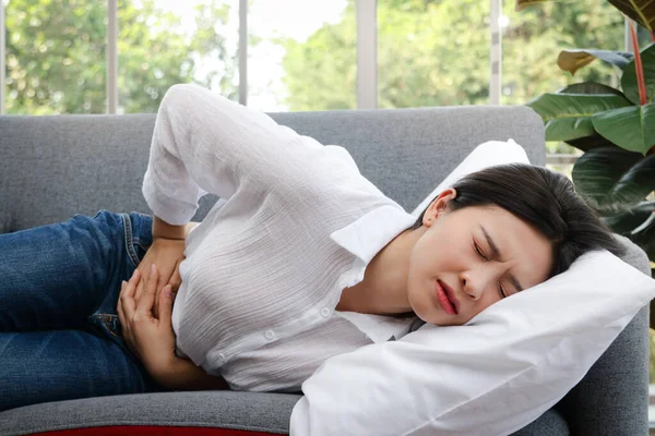 一位美丽的亚洲女人在家里的房间里躺在沙发上 肚子痛 妇女病征月经前疾病或腹痛的征兆 — 图库照片