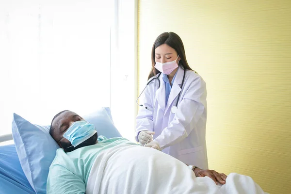 Μια Ασιάτισσα Γιατρός Φοράει Γάντια Ένεσης Έναν Αφροαμερικανό Ασθενή Ξαπλωμένο — Φωτογραφία Αρχείου