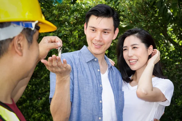 Asyalı erkek ve kadın çiftler ev teftişi mühendisinden ev anahtarlarını alıyorlar. Onların her ikisi de yeni evlerinden memnundu. Aile kurma kavramı.