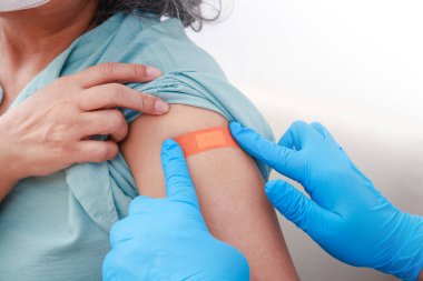 Enfeksiyonu önlemek için bağışıklık sistemini güçlendirmek için mavi eldiven giyen bir erkek doktordan koronavirüs aşısı alan yaşlı bir kadının yakın plan portresi. Yaşlılara Aşı