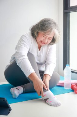 Evde egzersiz yapan Asyalı yaşlı kadın sağ ayak bileğinden yaralandı. Çok fazla acı var. Yaşlılar için sağlık hizmeti kavramı.