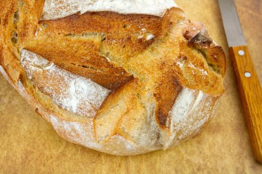 Tahta yüzeyde taze pişmiş beyaz ekmek ve yakınlarda bir bıçak..