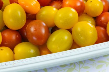 Sarı ve kırmızı domatesleri beyaz bir kasede yıkadı..