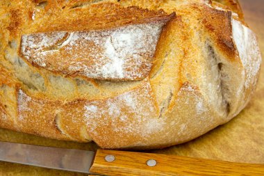 Tahta yüzeyde taze pişmiş beyaz ekmek ve yakınlarda bir bıçak..