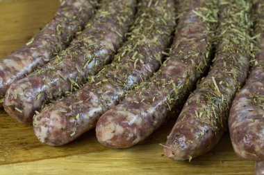 Ahşap kesme tahtasının üzerinde aromalı bitkilerle çiğ domuz sosisi..