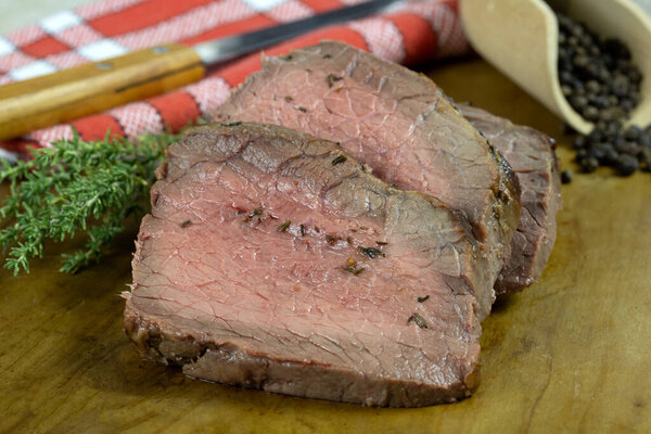 Delicious sliced beef steak with rosemary and pepper on wooden board