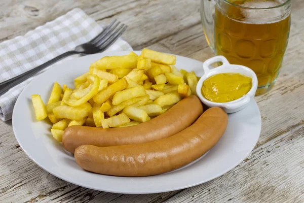 Sausages, French fries and mustard in a white plate.
