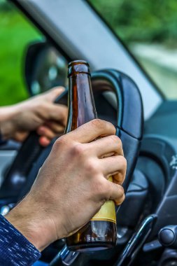Araba kullanan ve bira içen bir adamın yakın çekimi. Şişeli ve direksiyonlu bir erkek eli. 