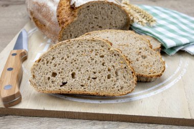 Bir somun ekmek ve birkaç dilim un, tahta kesme tahtasının üzerinde..