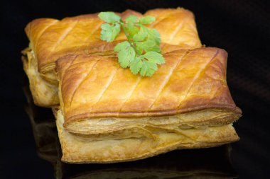 Peynirli fırında börek ve siyah arka planda maydanoz. 