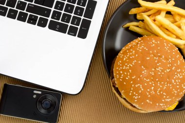 Çizburger ve patates kızartması laptopun yanında.