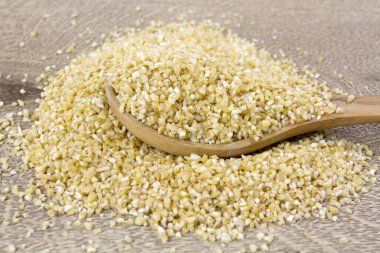 Tahta arka planda tahta kaşıkta bulgur.