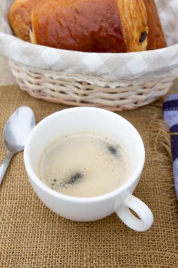 Bir fincan kahve ve bir sepet çörekler ahşap bir masada.