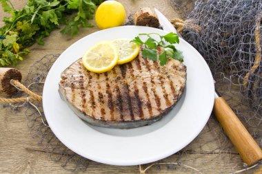 Ahşap bir masada limonlu ızgara balık ve otlar.