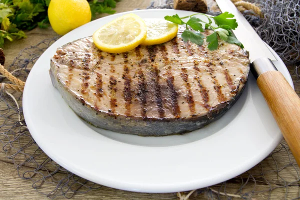 Ahşap bir masada limonlu ızgara balık ve otlar.