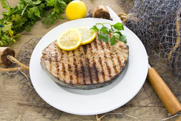 Ahşap bir masada limonlu ızgara balık ve otlar.