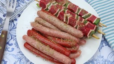 Bir tabak sosis, merguez ve çiğ biftek şişleri.