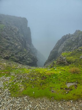 Bulutlu mavi gökyüzünün altında yeşil tepeleri olan doğal İskoç manzarası