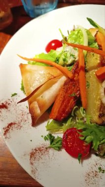 Bir tabak çıtır samosa yanında vişneli domates, havuç, soğan ve otla taze bir salata. Restoran masasında renkli ve iştah açıcı bir sunumla sunuluyor..