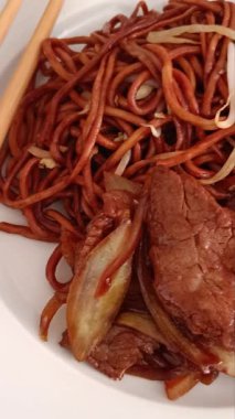 Kızarmış erişteyle servis edilen soğanlı biftek, iştah açıcı.