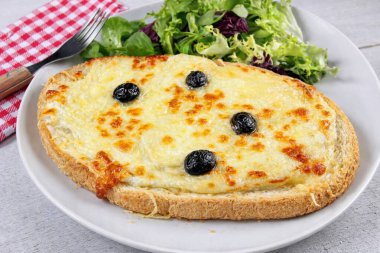 Peynirli ve siyah zeytinli kızarmış pizza, yeşil salatayla servis edilir.