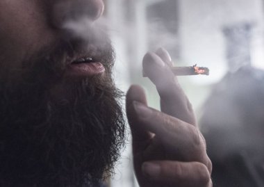 Sakallı bir adam sarılmış sigara içiyor.