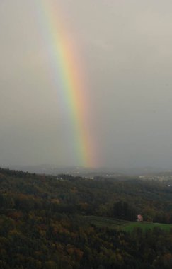 Bir yaz gününde renkli gökkuşağı, arka planda orman ve tepe