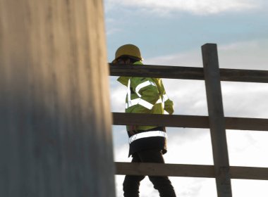 construction worker in safety clothing walking behind a wooden fence at the construction site