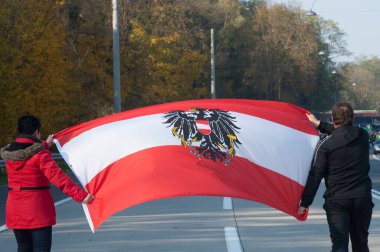 Kırmızı kırmızı Avusturya bayrağı taşıyan insanlar sokakta yürüyorlar.