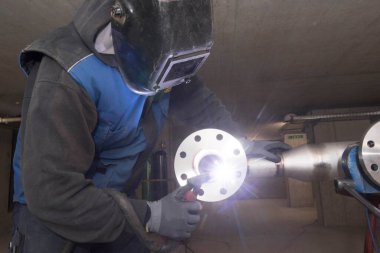 Metal işçisi koruyucu giysiler içinde bir boru kaynak yapıyor.