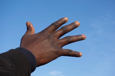 Arka planda mavi gökyüzü olan siyah bir insanın eli