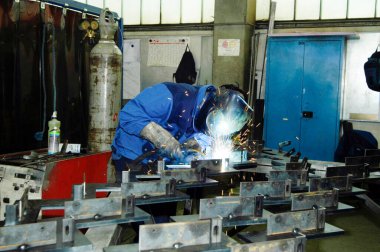 Metal işçisi koruyucu giysiler içinde bir boru kaynak yapıyor.