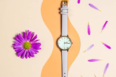 Bej bir arka planda çiçek yapraklarıyla bej bir kayışı olan kadın saati.