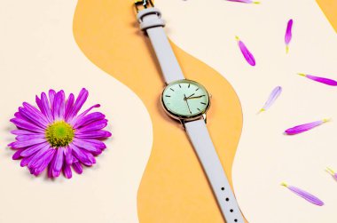 Bej bir arka planda çiçek yapraklarıyla bej bir kayışı olan kadın saati.