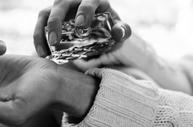 Genç bir kadın bileğine siyah beyaz parfüm serpiyor.