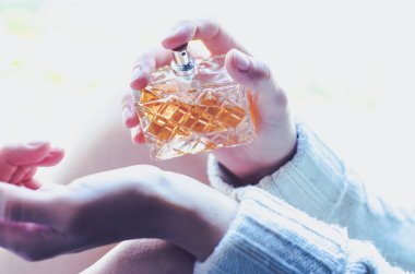 Genç bir kadın bileğine parfüm serpiyor. Bir kadının elindeki parfüm