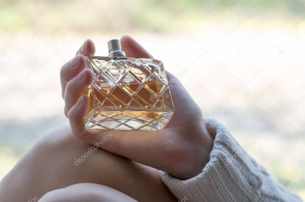 A woman holds a bottle of perfume in her hands. Perfume in a woman's hand