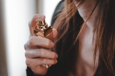 Genç ve güzel bir kadın parfüm kullanıyor. Kadın ellerinde parfüm şişesi