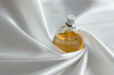 İpek kumaşlı parfüm. Dalgalı ipeğe sarılmış bir kadın parfümü şişesi