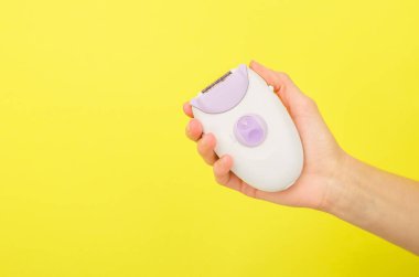 Sarı arkaplandaki bir kadın elinde, mesaj için yeri olan bir epilatör.