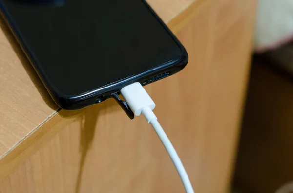 The charger is connected to the smartphone. The phone is on the edge of the table