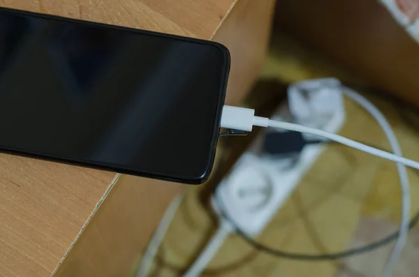 The charger is connected to the smartphone. The phone is on the edge of the table