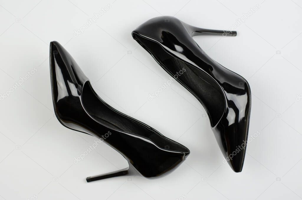 A pair of black patent women's shoes on a gray background. Women's stiletto heels