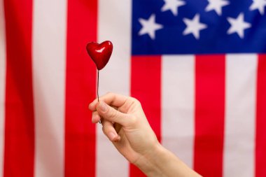 Kırmızı kalp, Amerikan bayrağının arka planına karşı kadının ellerinde.