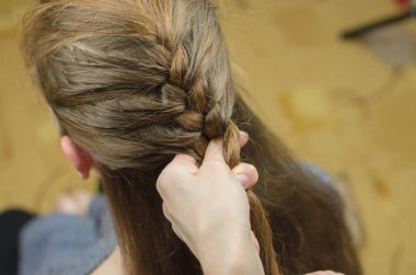 Kızıl saçlı bir kız için örgü ören bir kadın. Saç dokuma stili. Örgü örüyorum.