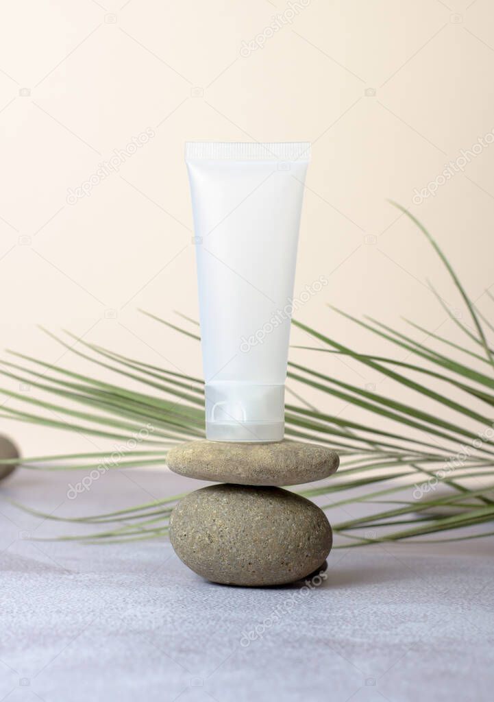 White empty tube for cream on the stone. Mockup tube on beige background with green leaf