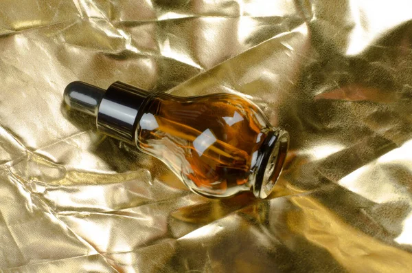 Altın arka planda bir damlatıcıyla cam şişedeki kozmetik yağı. Doğal vücut yağı şişesi. Cam şişedeki serum..