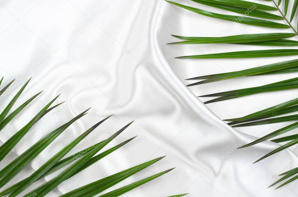 Beautiful background of white silk fabric with green palm branches. Wavy fabric texture with place for text