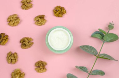 Krema kavanozu, ceviz ve pembe arka planda bir tutam okaliptüs. Cilt bakımı için organik kozmetik. Damgalamak ve etiketlemek için bir şişe.