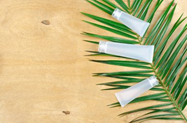 Krema için beyaz tüpler ve ahşap arka planda yeşil yapraklar. Cilt bakımı için organik kozmetik ürünleri.